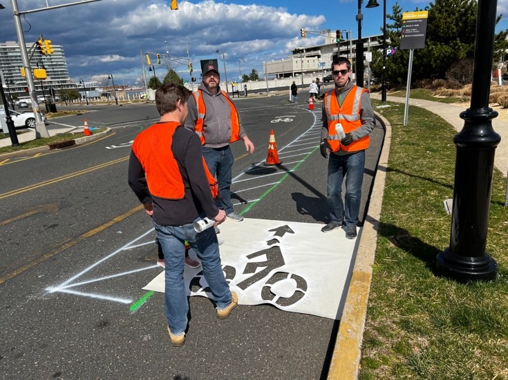 Students and an instructor from the Bloustein School at Rutgers install a temporary bike lane made from stencils and chalk in Asbury Park, NJ. Data gathered before and during the demonstration showed that the bike lane reduced vehicle speeds at the nearby intersection, reducing crash risk and increasing safety not only for bicyclists, but also pedestrians and people in vehicles. (Source: NJDOT Bicycle & Pedestrian Resource Center)